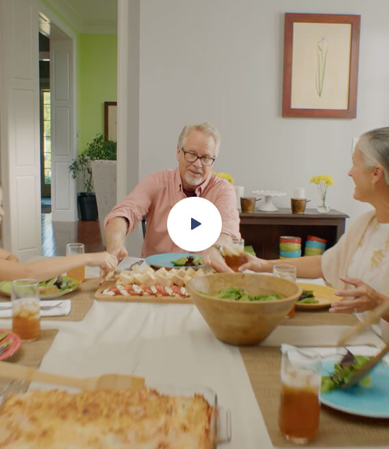 Man passing salad bowl to other people eating at a dinner table
