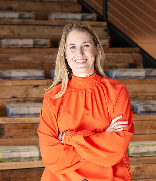 Woman in an orange shirt standing in front of wooden stairs
