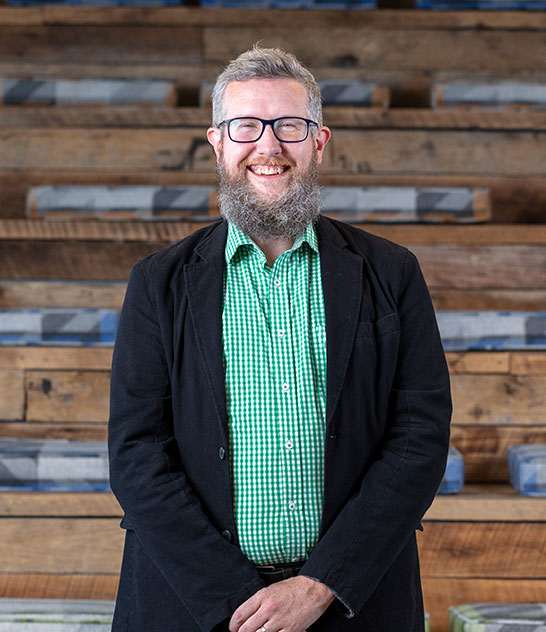 Man with beard and glasses standing in front of wooden stairs